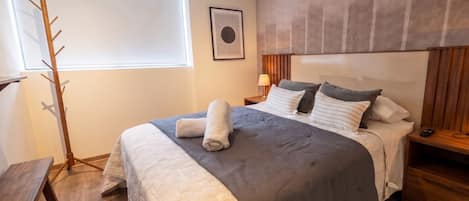 Un dormitorio con cama, mesitas de noche, lámpara, perchero y ventana.
