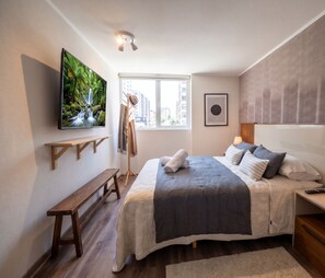 A bedroom with a bed, a TV, a window, and a bench. - Edificio Status Santiago by Domus Travels (Santiago)