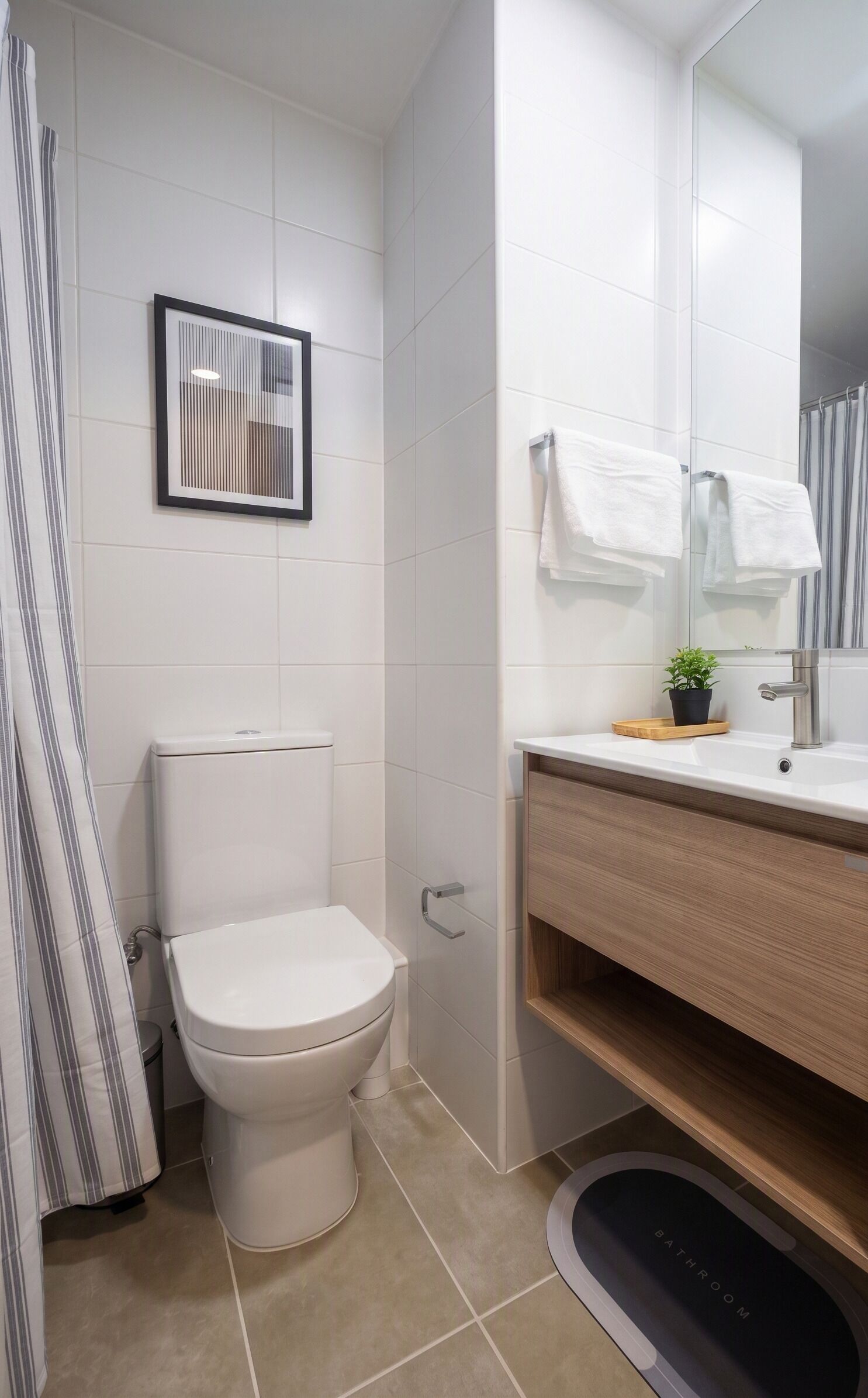 A modern bathroom with a toilet, a shower curtain, a sink with a mirror, and a small potted plant.