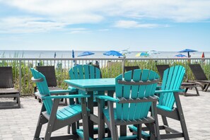 A patio with turquoise Adirondack chairs and a table, overlooking a beach with umbrellas. - Modern 2BR Oceanfront Condo w/ Balcony at Oceans One (Myrtle beach)
