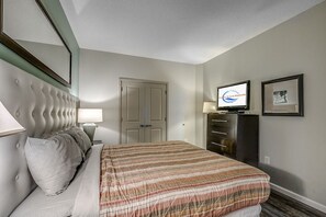 A hotel room with a bed, a television, a dresser, and a door. - Modern 2BR Oceanfront Condo w/ Balcony at Oceans One (Myrtle beach)