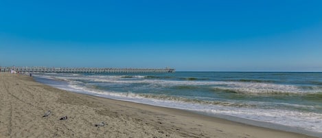 A beach with a pier extending into the water, sandy shore, and a clear sky.