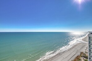 A beach with a clear sky, a building with balconies, and a calm sea. - Modern 2BR Oceanfront Condo w/ Balcony at Oceans One (Myrtle beach)