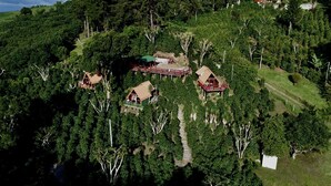 An aerial view of a forested area with several small, elevated wooden structures, likely cabins or lodges, connected by pathways.