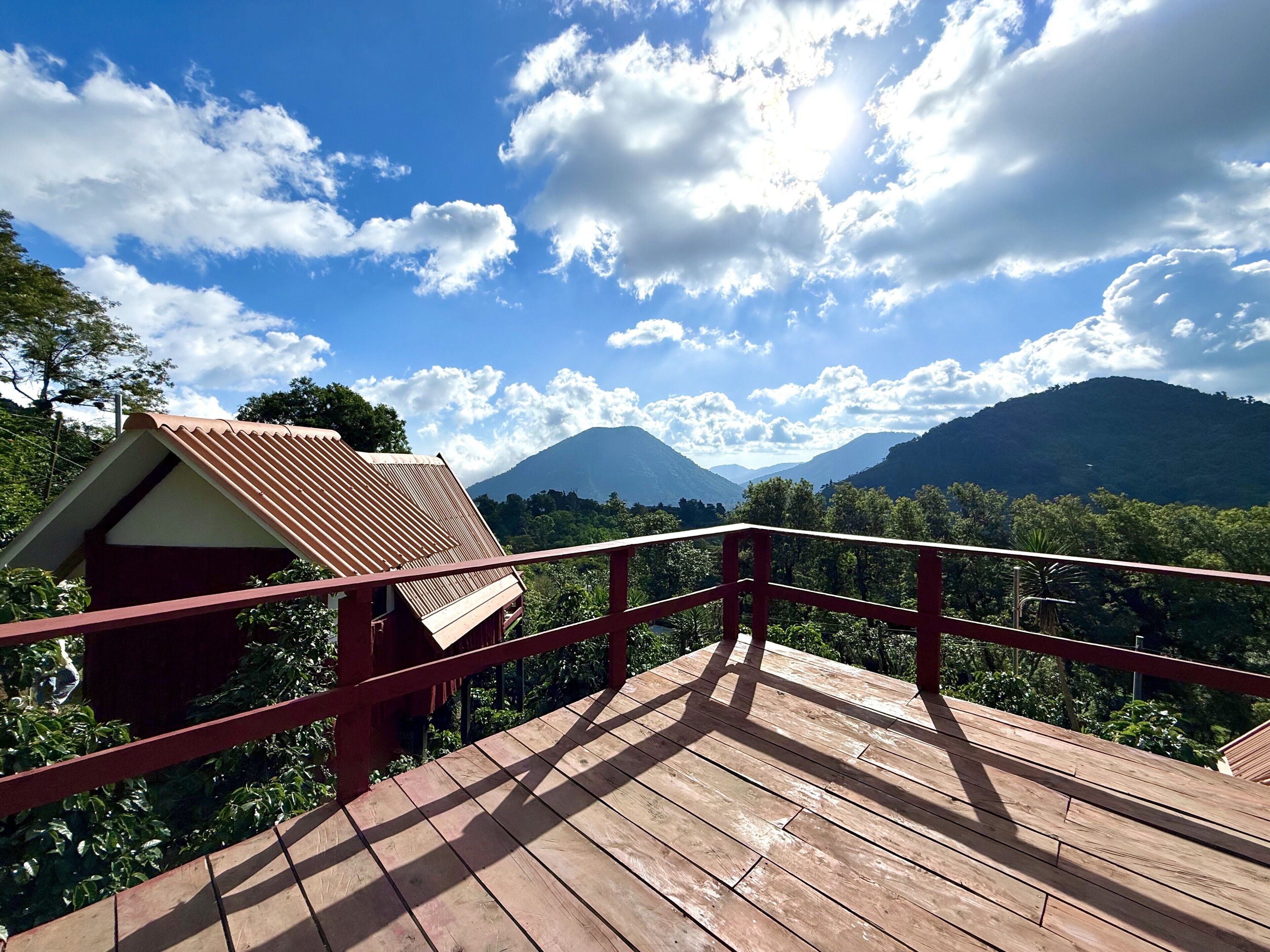 En træterrasse med rødt gelænder, der kigger ud over et bjergrigt landskab med en klar himmel.