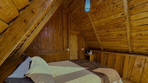 A wooden room with a sloped ceiling, a bed with a quilt, a nightstand, and a wall-mounted shelf with items.