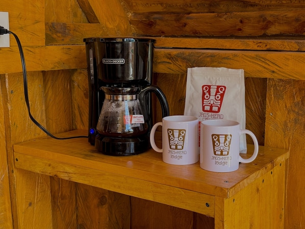 Une machine à café, deux tasses et un sac posés sur une étagère en bois.