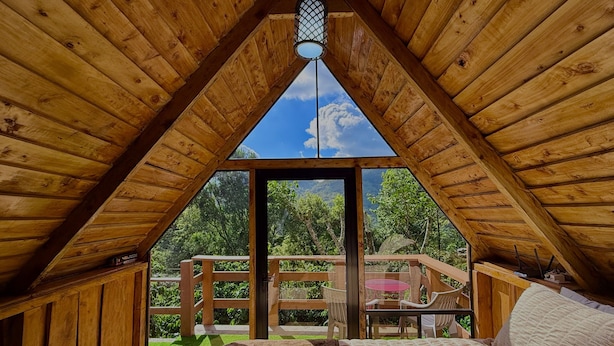 A wooden attic bedroom with a view of a balcony and greenery.