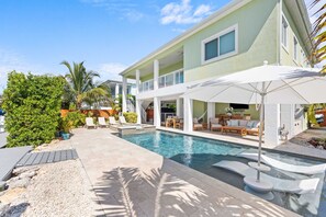 A pool area with a lounge, umbrellas, and outdoor furniture. - Emerald Palms Waterfront Pool Dock Games (Marathon)