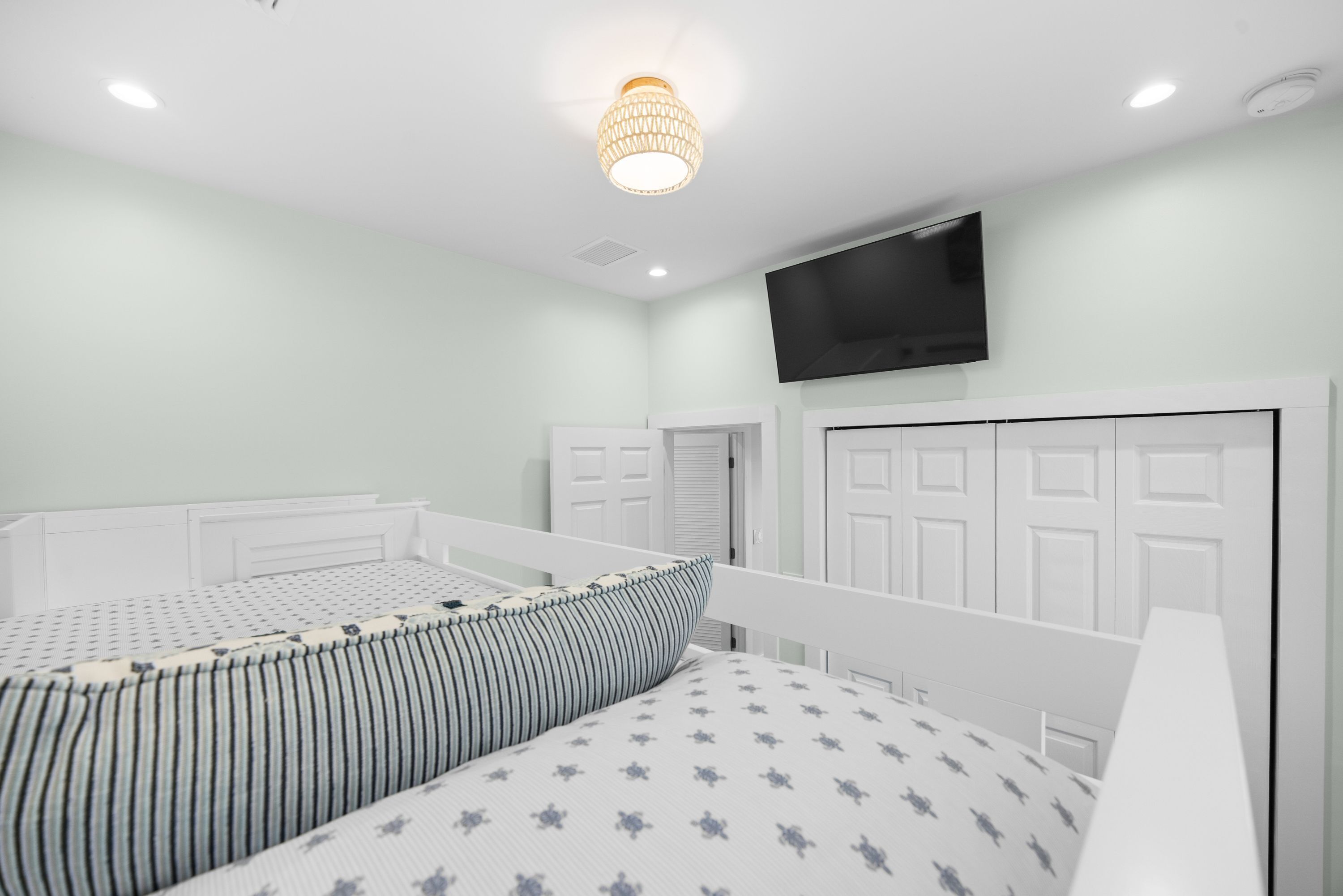 A bedroom with two single beds, a television mounted on the wall, and a door with a handle.