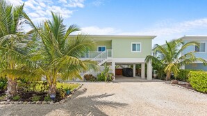 A two-story house with a covered porch, a gravel driveway, and palm trees. - Emerald Palms Waterfront Pool Dock Games (Marathon)