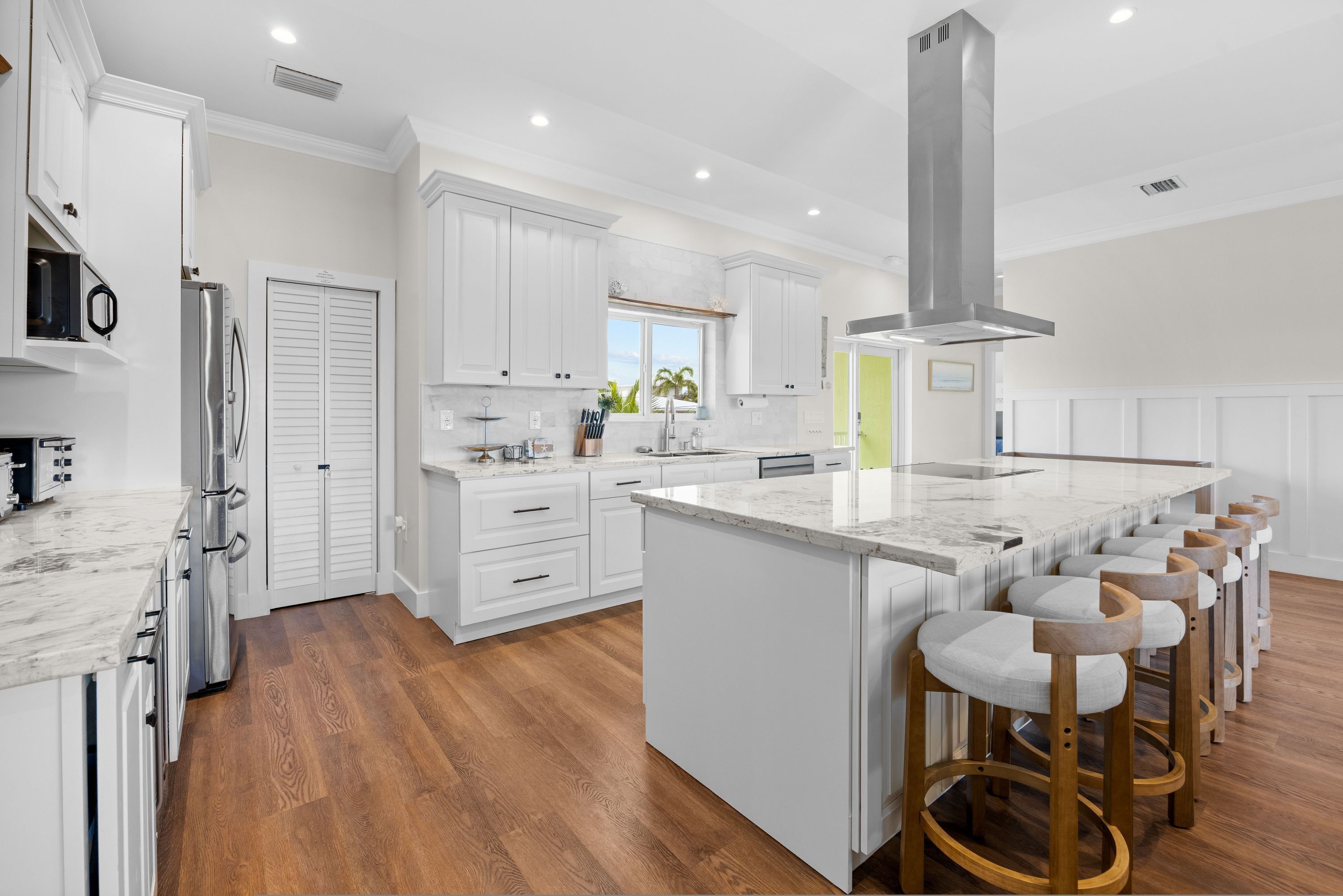 A modern kitchen with white cabinetry, a large island with bar stools, and a view of the outdoors.