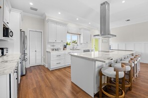 A modern kitchen with white cabinetry, a large island with bar stools, and a view of the outdoors. - Emerald Palms Waterfront Pool Dock Games (Marathon)