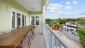 A balcony with a wooden table and chairs, a view of a marina with boats, and a clear sky. - Emerald Palms Waterfront Pool Dock Games (Marathon)
