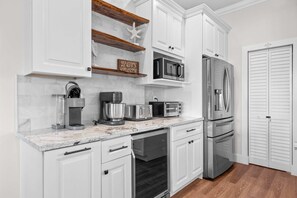 Eine moderne Küche mit weißen Schränken, einer eingebauten Mikrowelle, einem Edelstahl-Kühlschrank und einer Kaffeemaschine.