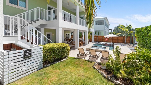 A two-story building with a pool area, outdoor seating, and a staircase. - Emerald Palms Waterfront Pool Dock Games (Marathon)