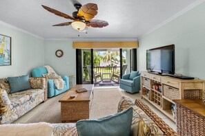 A living room with a ceiling fan, a television, a sofa, a coffee table, and a wicker side table. - Sandbar Serenade Private Beach Heated Pool Key Colony Beach (Key Colony Beach)