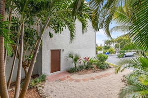 A building with a white exterior, a brown door, and a gravel pathway leading to it. - Sandbar Serenade Private Beach Heated Pool Key Colony Beach (Key Colony Beach)