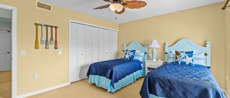 A bedroom with two beds, a ceiling fan, a closet, and wall-mounted items.