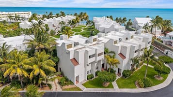 A residential complex with multiple white buildings, palm trees, and a view of the ocean.
