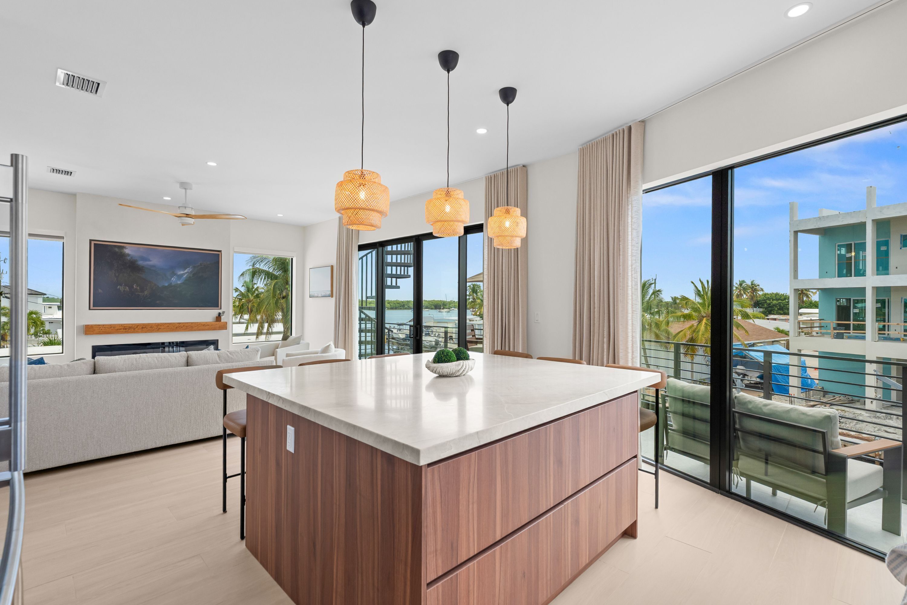 A modern kitchen with a central island, a dining area with a view, and a living room with a large TV.