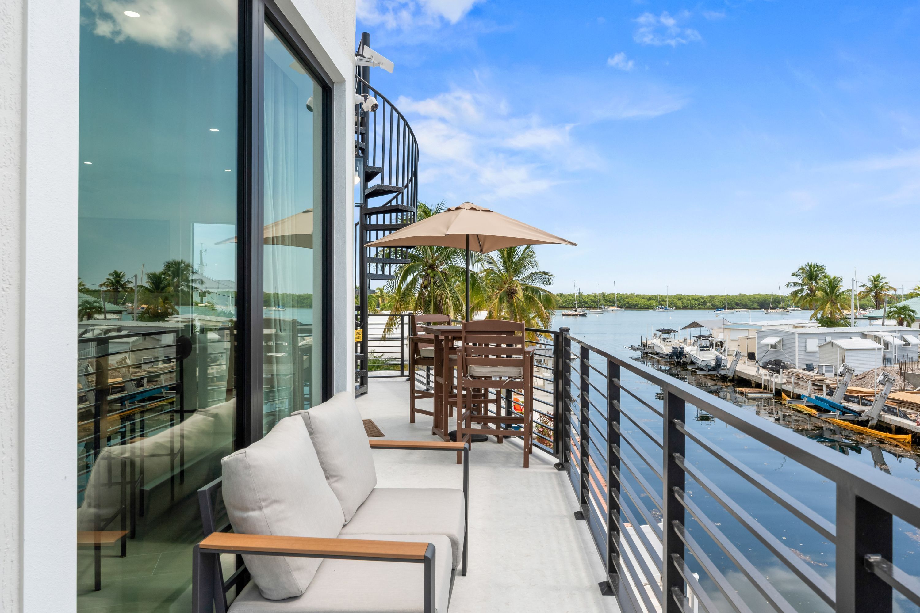 Varanda com sofá, mesa e guarda-sol, com vista para uma marina e barcos.