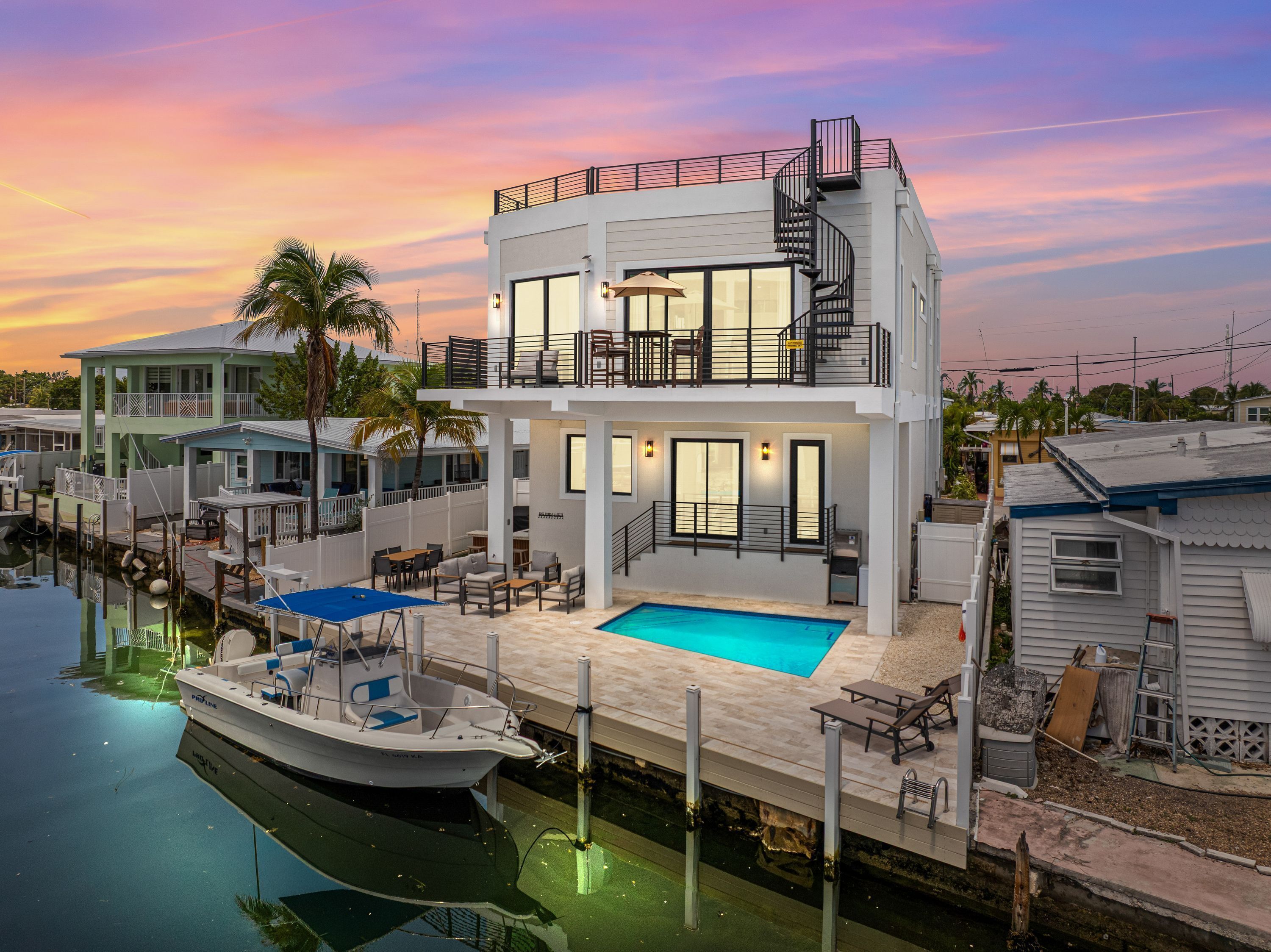 A two-story waterfront property with a pool, dock, and outdoor seating area.