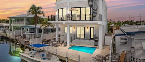 A two-story waterfront property with a pool, dock, and outdoor seating area.