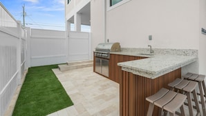 A modern outdoor kitchen with a grill, bar stools, and a small sink. - Cielo del Mar - Waterfront - Heated Pool - Dock (Marathon)