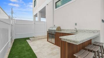 A modern outdoor kitchen with a grill, bar stools, and a small sink.