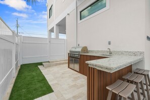 A modern outdoor kitchen with a grill, bar stools, and a small sink. - Cielo del Mar - Waterfront - Heated Pool - Dock (Marathon)