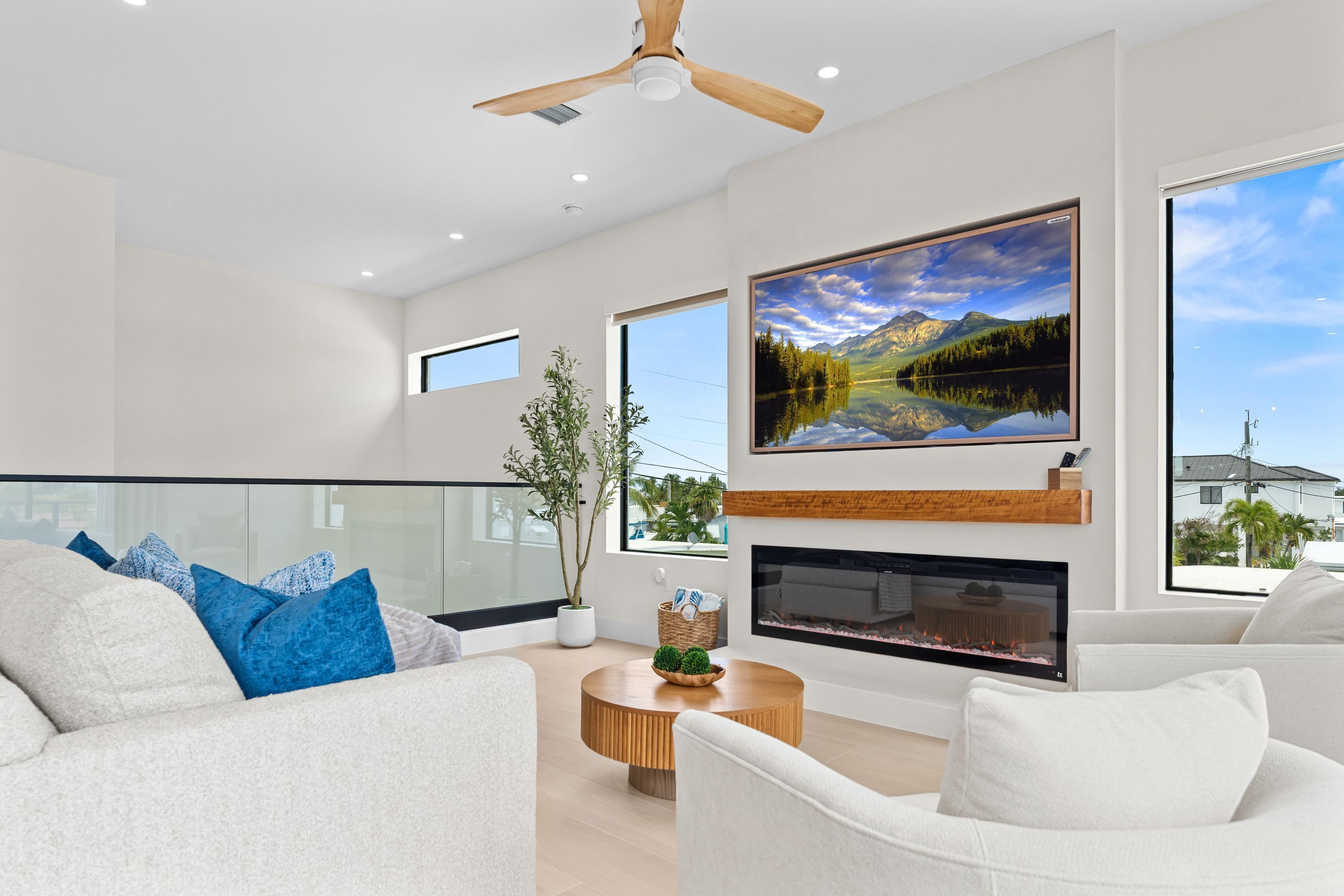 A modern living room with a fireplace, a large window with a mountain view, and a ceiling fan.