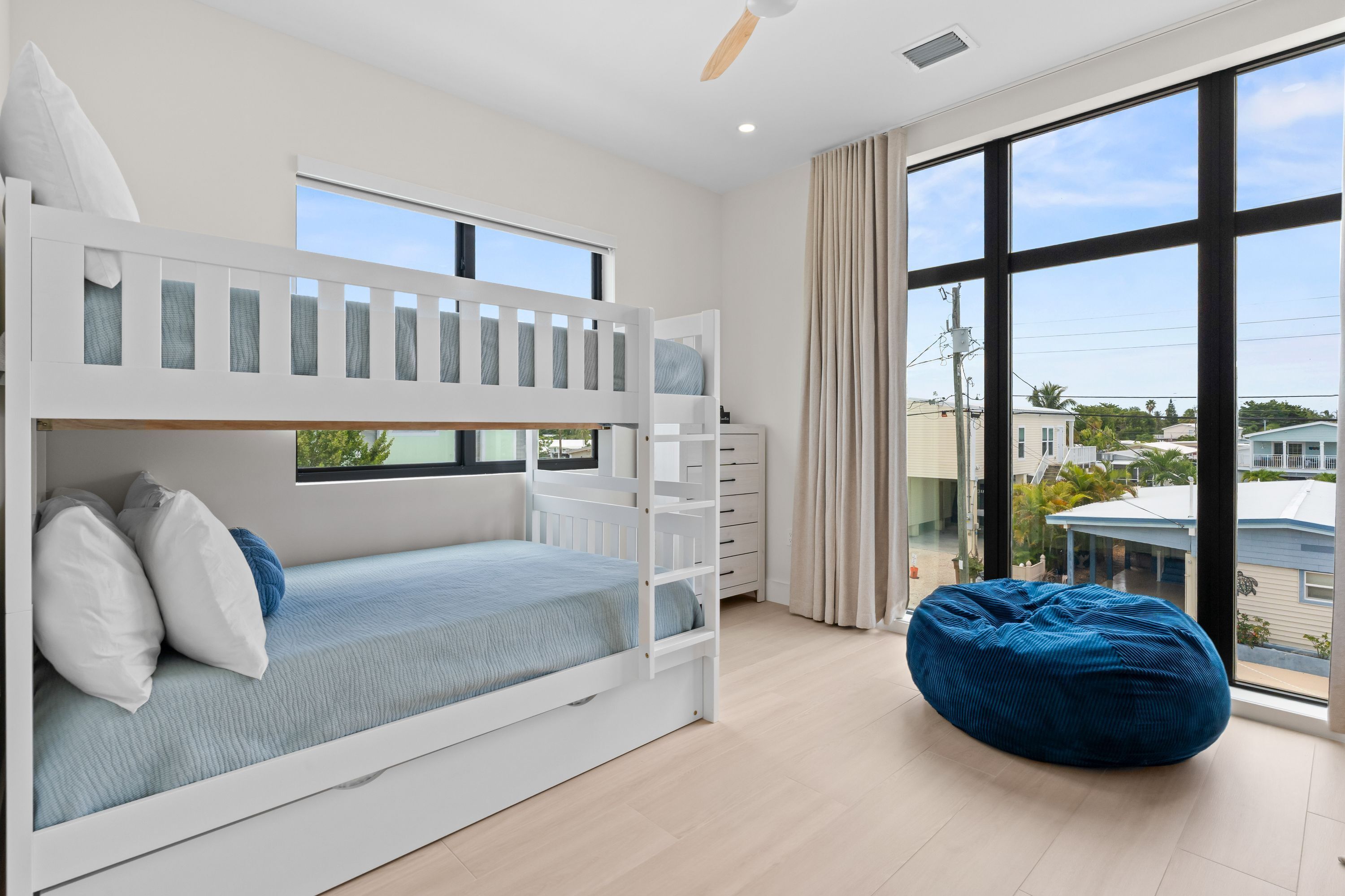 A room with a bunk bed, a bean bag chair, and a large window offering a view of the outside.