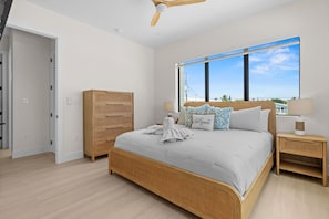 A bedroom with a large bed, a wooden wardrobe, a nightstand with a lamp, and a window with a view of the sky. - Cielo del Mar - Waterfront - Heated Pool - Dock (Marathon)