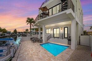 A two-story building with a swimming pool, outdoor seating, and a view of a marina. - Cielo del Mar - Waterfront - Heated Pool - Dock (Marathon)