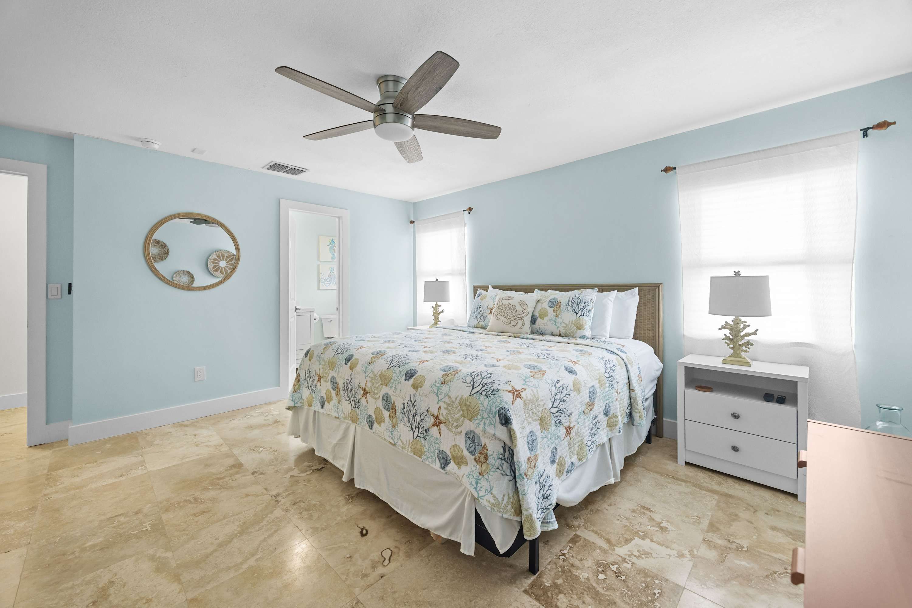 A bedroom with a bed, a nightstand, a ceiling fan, a window with curtains, and a wall-mounted mirror.