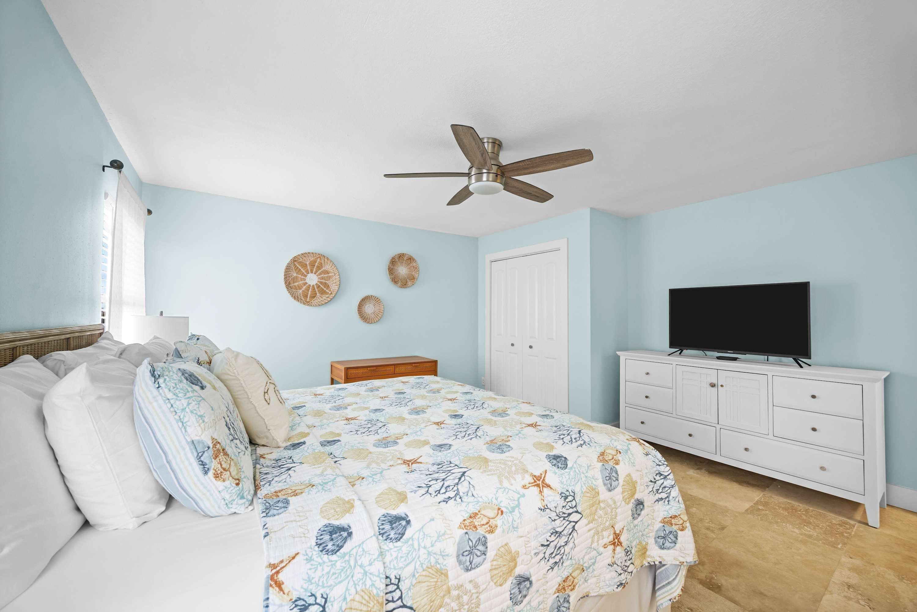 A bedroom with a bed, a ceiling fan, a dresser, a television, and decorative wall art.