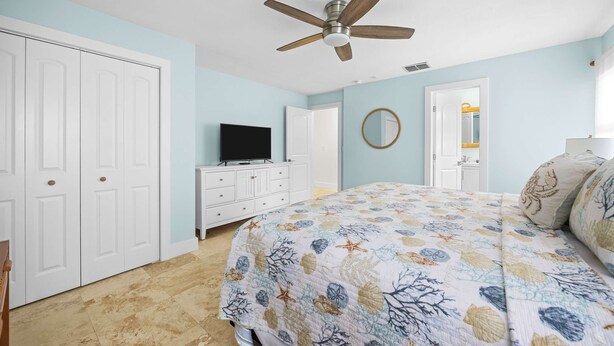 A bedroom with a bed, a ceiling fan, a television on a dresser, and a door. - Catch of the Bay - Waterfront - Pool - 35 Dock (Marathon)