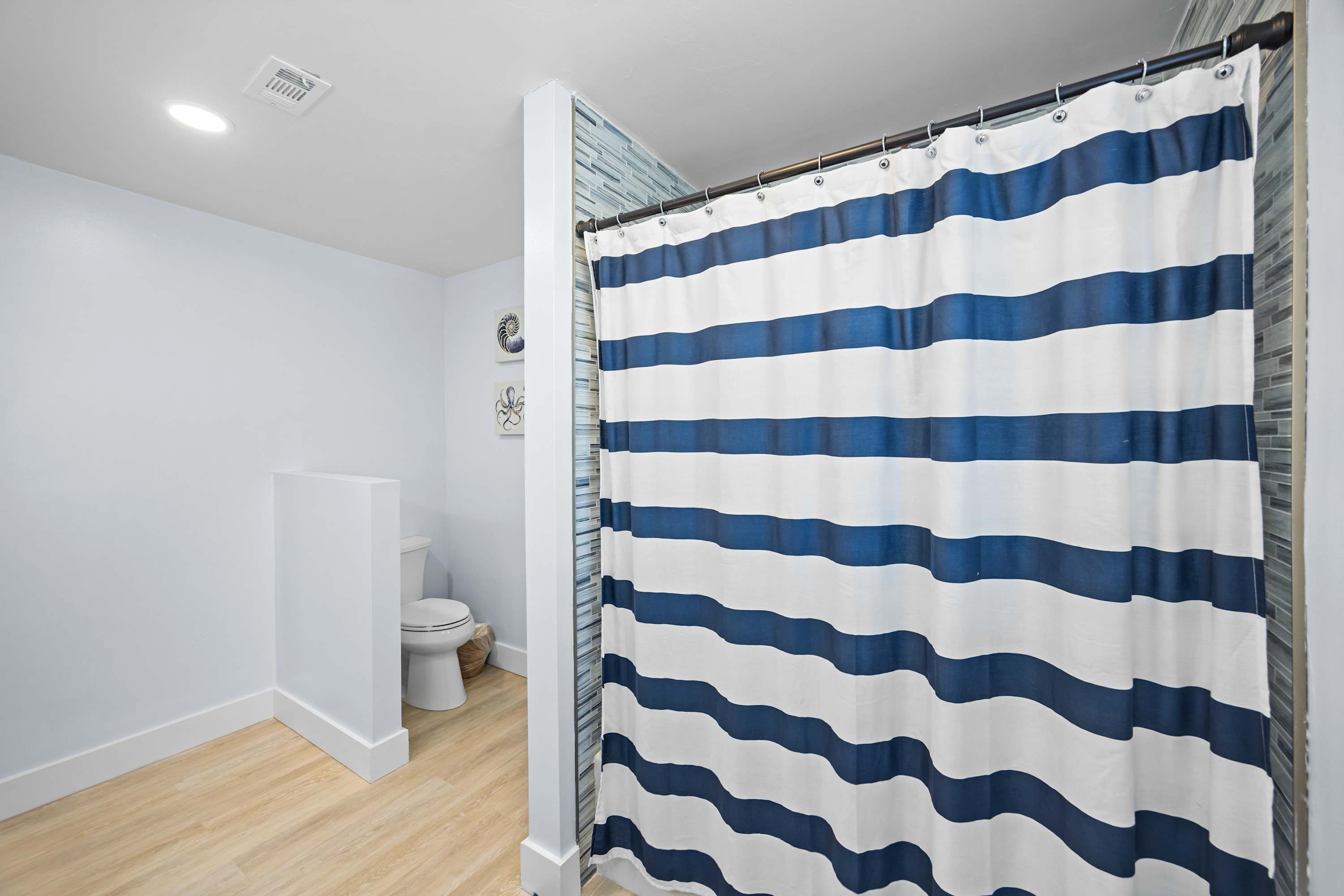 Une salle de bain avec un rideau de douche à rayures horizontales bleues et blanches, des toilettes blanches et un plancher en bois.