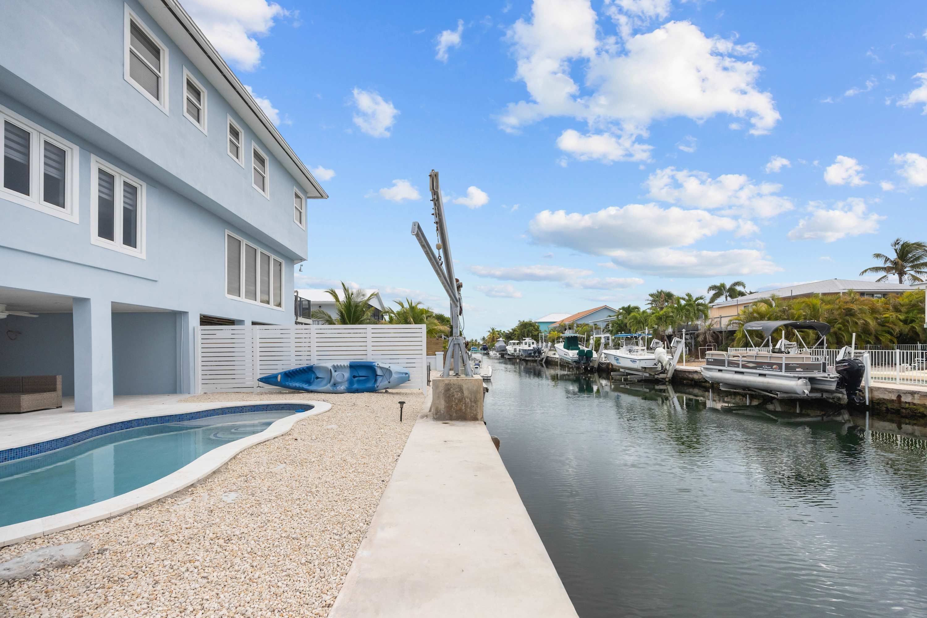 Una propiedad frente al agua con piscina, un muelle con barcos y un edificio blanco con amplias ventanas.