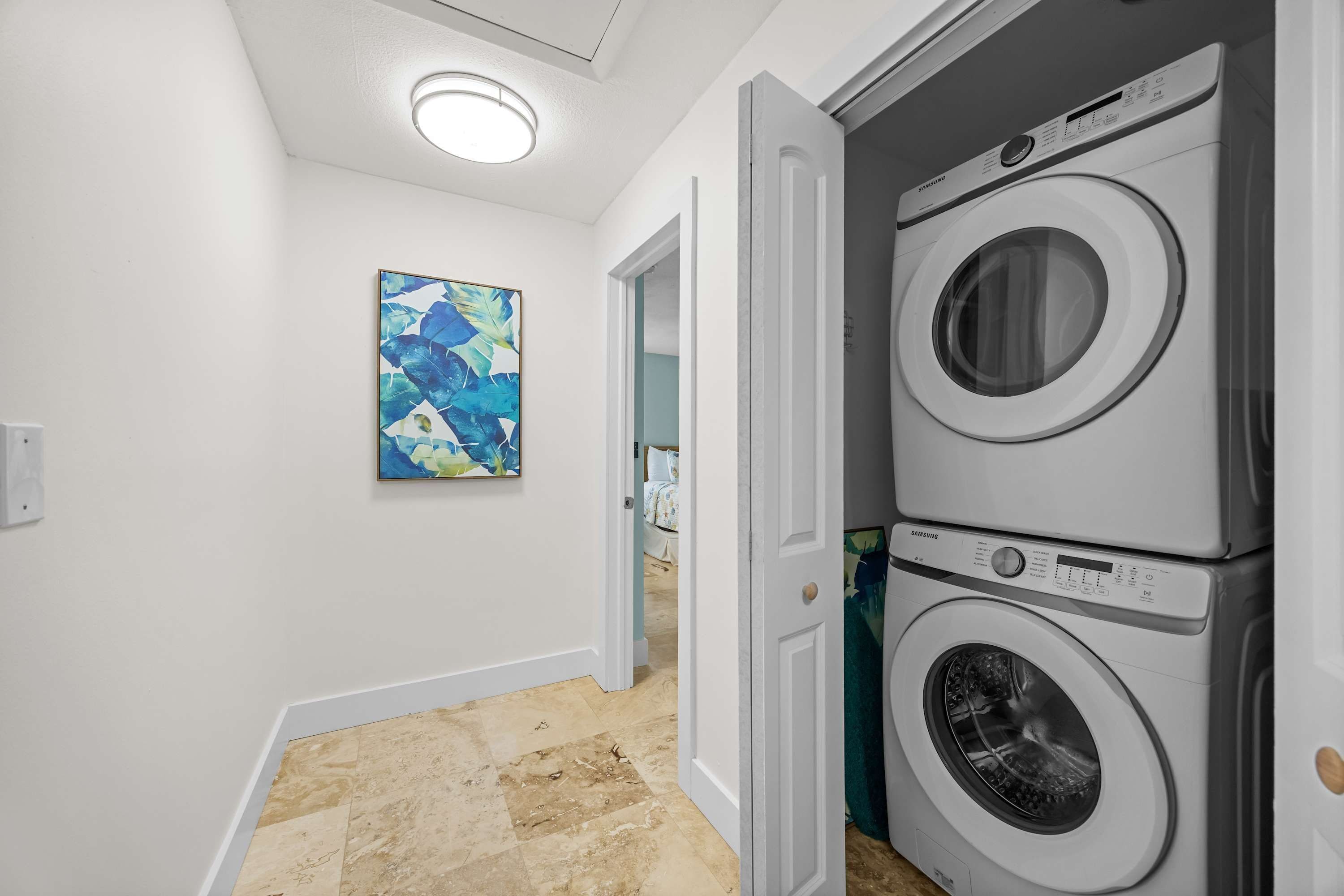 A laundry room with two stacked front-loading washers and dryers, a door leading to another room, and a ceiling light.
