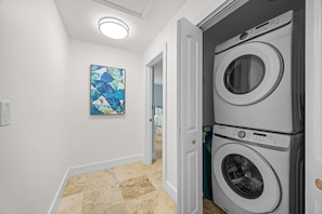 A laundry room with two stacked front-loading washers and dryers, a door leading to another room, and a ceiling light. - Catch of the Bay - Waterfront - Pool - 35 Dock (Marathon)