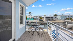A balcony with a table and chairs, overlooking a marina with boats and houses. - Catch of the Bay - Waterfront - Pool - 35 Dock (Marathon)