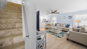 A modern living room with a staircase, a ceiling fan, and a kitchen in the background. - Catch of the Bay - Waterfront - Pool - 35 Dock (Marathon)