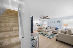 A modern living room with a staircase, a ceiling fan, and a kitchen in the background. - Catch of the Bay - Waterfront - Pool - 35 Dock (Marathon)