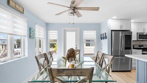 A modern kitchen with a glass dining table, wooden chairs, stainless steel appliances, and a ceiling fan. - Catch of the Bay - Waterfront - Pool - 35 Dock (Marathon)