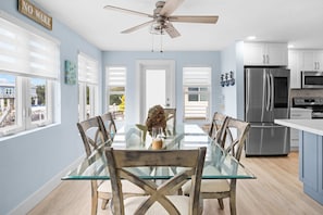 A modern kitchen with a glass dining table, wooden chairs, stainless steel appliances, and a ceiling fan. - Catch of the Bay - Waterfront - Pool - 35 Dock (Marathon)