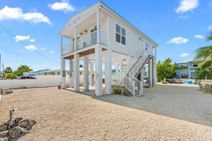 Ein zweistöckiges Strandhaus mit überdachter Veranda, einer Treppe und Blick auf den Ozean.