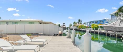 A wooden dock leading to a marina with boats, a pool, and buildings with balconies.