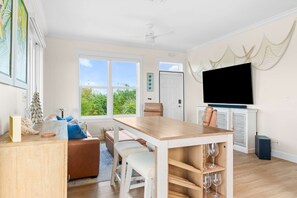 Ein geräumiges Wohnzimmer mit großem Fernseher, einem Essbereich mit Holztisch und Blick auf Grün.